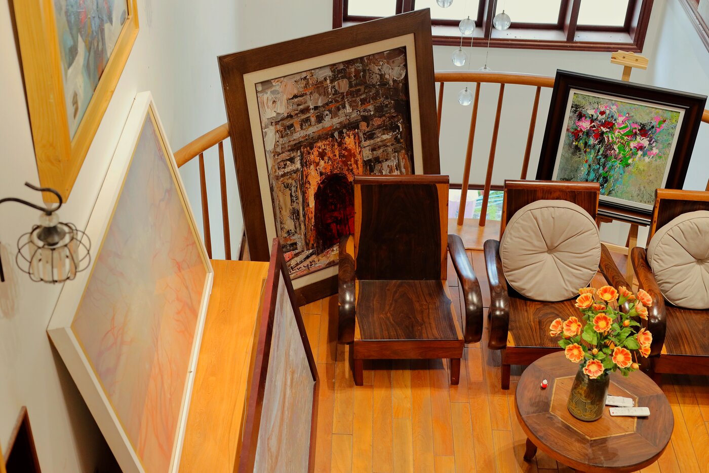 Góc đọc trên gác xép Nhung Art Space với ghế gỗ, tranh dựa tường, bàn trà và hoa hồng cam
